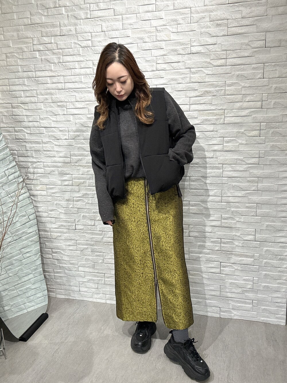 ブラック系のダウンベスト、グレー系のニット/セーター、イエロー系のスカートを着用したレディースの冬コーディネートの2枚目の写真