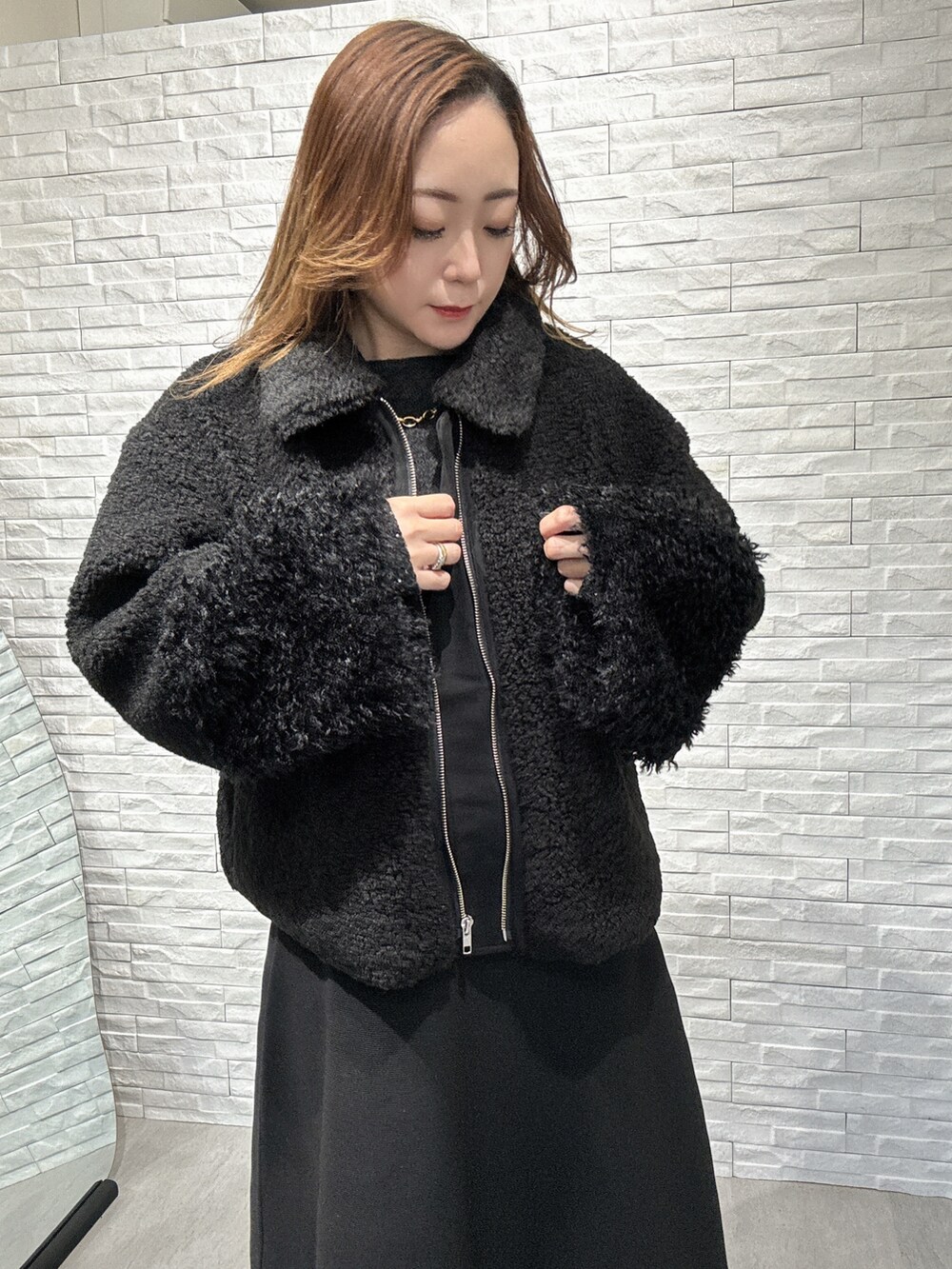 ブラック系のムートンコート、グレー系のニット/セーター、ブラック系のスカートを着用したレディースの冬コーディネートの2枚目の写真