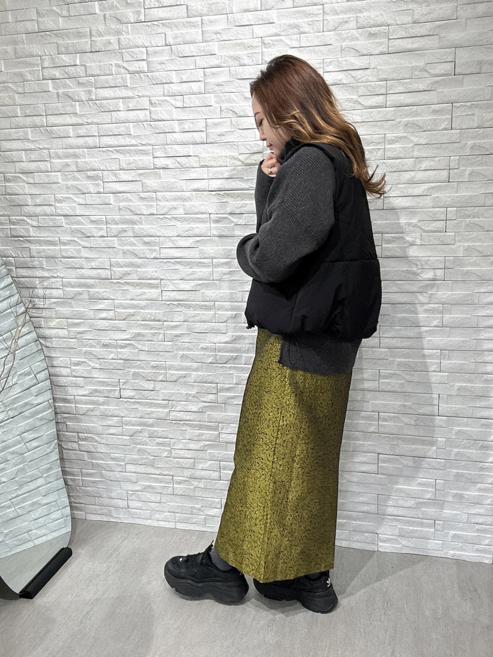 ブラック系のダウンベスト、グレー系のニット/セーター、イエロー系のスカートを着用したレディースの冬コーディネートの4枚目の写真
