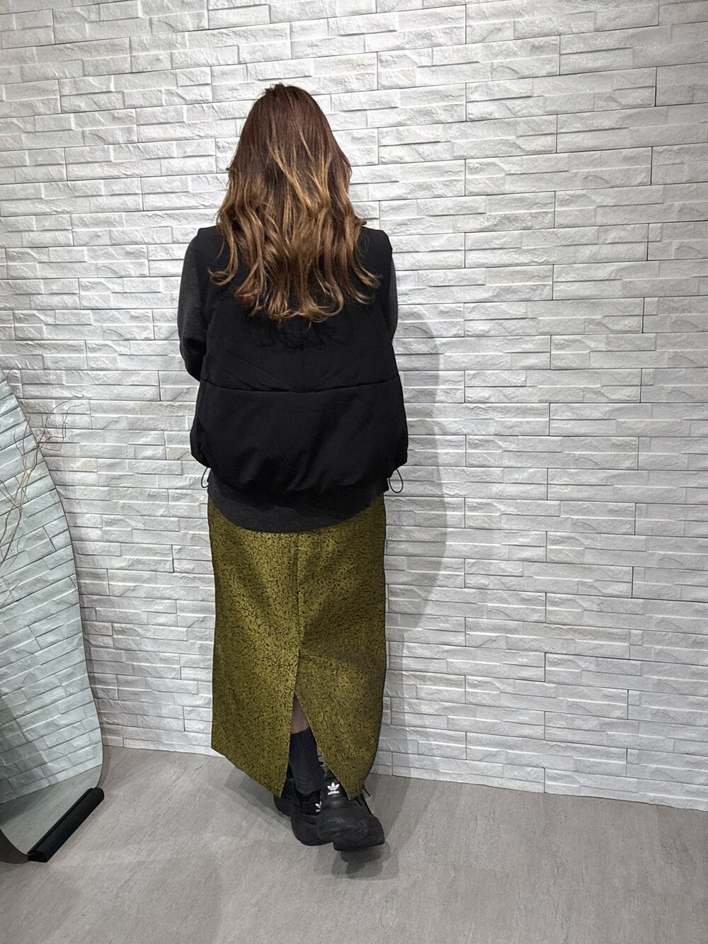 ブラック系のダウンベスト、グレー系のニット/セーター、イエロー系のスカートを着用したレディースの冬コーディネートの3枚目の写真