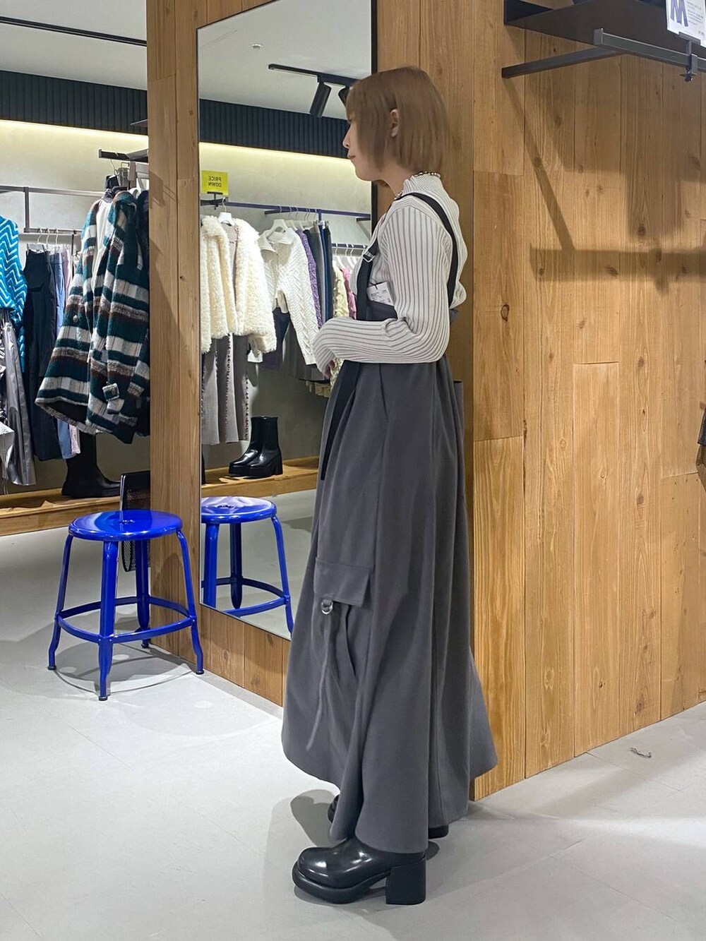 グレー系のジャンパースカート、ブラック系のブーツ、ホワイト系のニット/セーターを着用したレディースの冬コーディネートの2枚目の写真