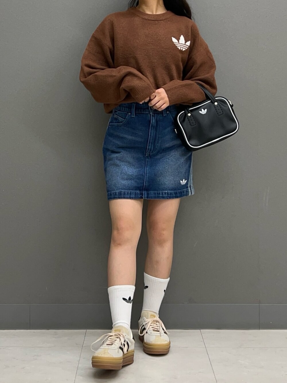 ブラウン系のニット/セーター、ブルー系のデニムスカート、ホワイト系のスニーカーを着用したレディースの秋コーディネートの2枚目の写真