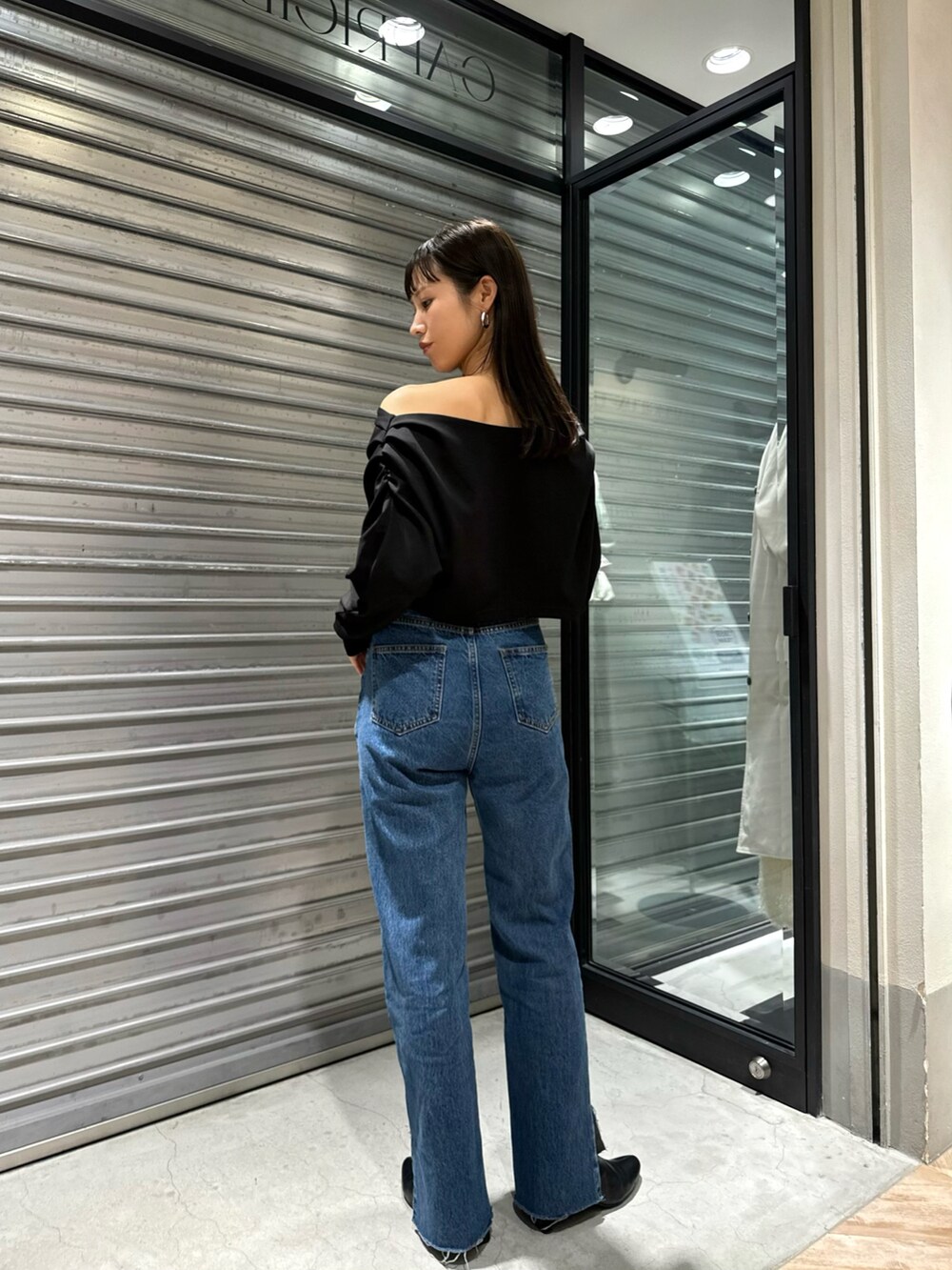 ブラック系のワンピース、ブルー系のデニムパンツ、ブラック系のブーツを着用したレディースの春コーディネートの2枚目の写真