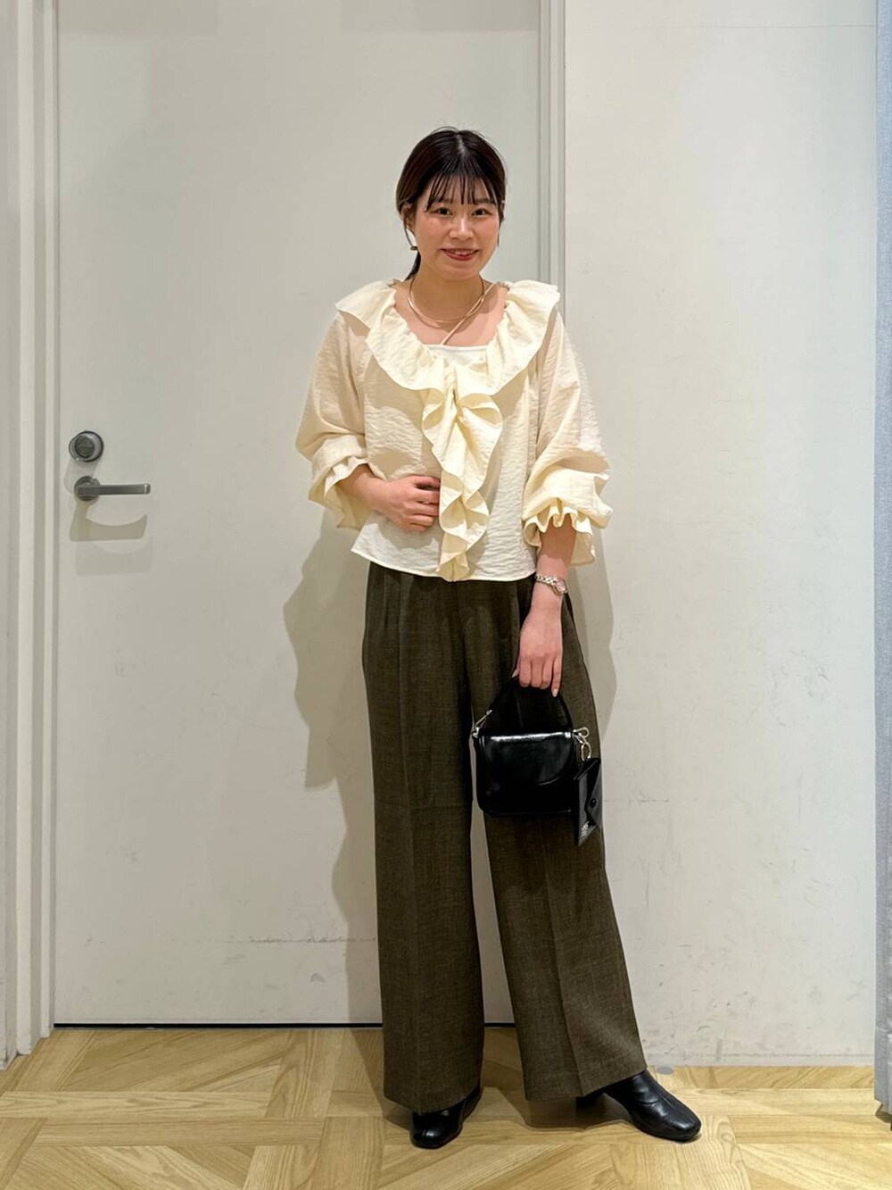 ブラック系のブーツ、ブラウン系のスラックス、ホワイト系のキャミソールを着用したレディースの春コーディネートの2枚目の写真