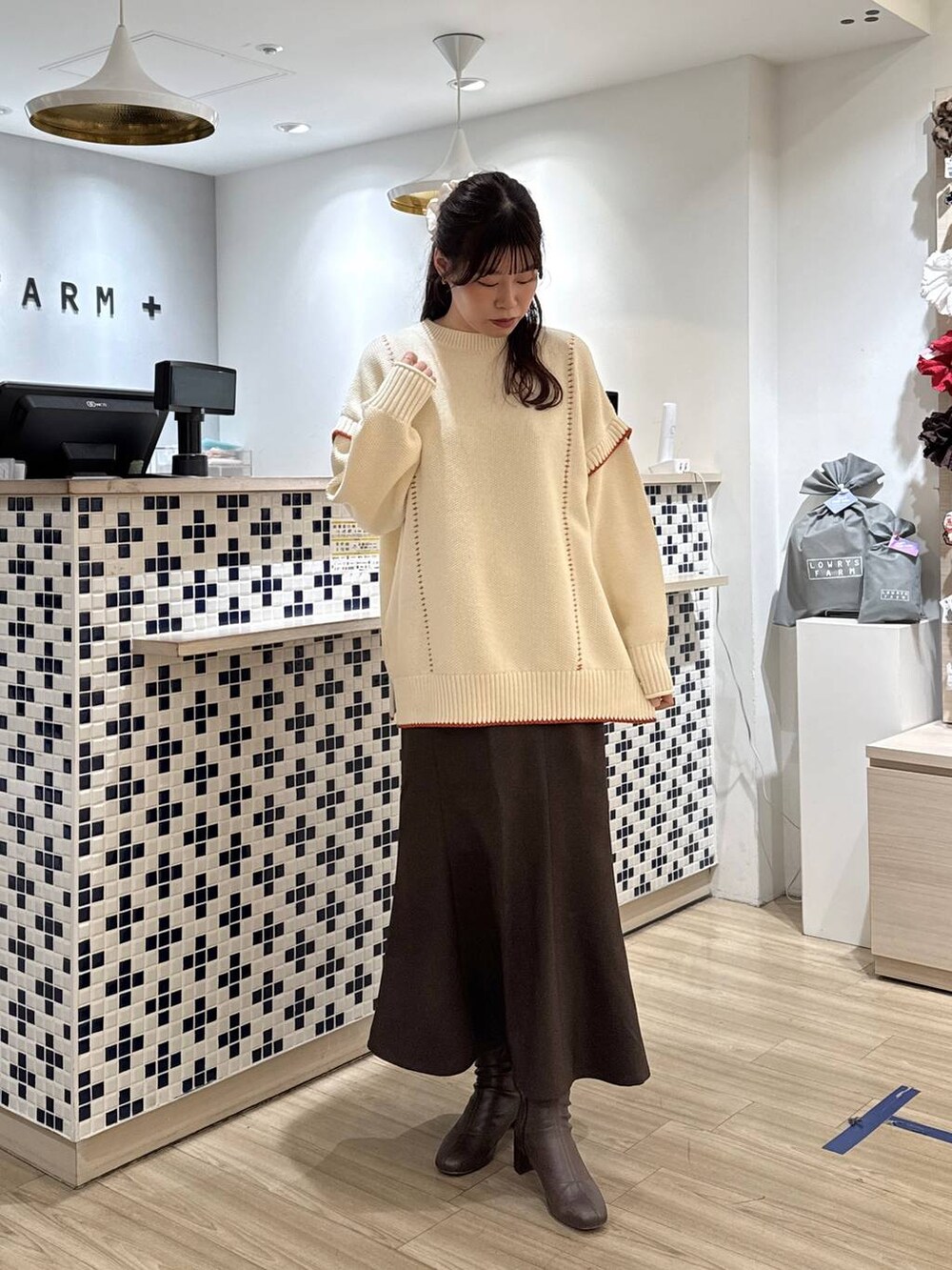 ホワイト系のニット/セーター、ブラウン系のスカート、ブラウン系のブーツを着用したレディースの冬コーディネートの2枚目の写真