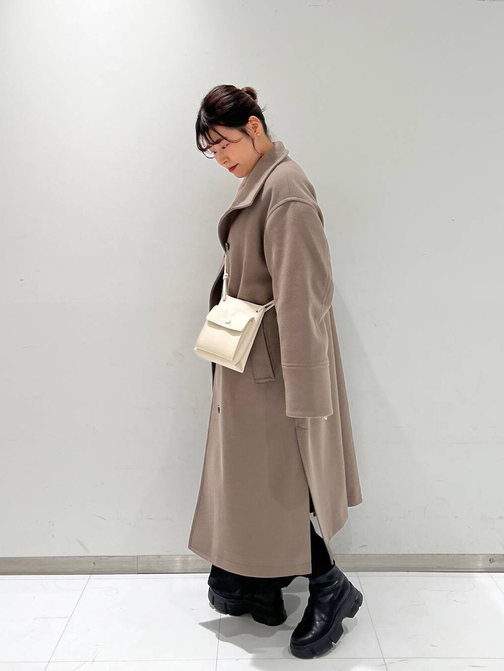 ホワイト系のショルダーバッグ、ブラウン系のチェスターコート、ブラック系のブーツを着用したレディースの冬コーディネートの2枚目の写真