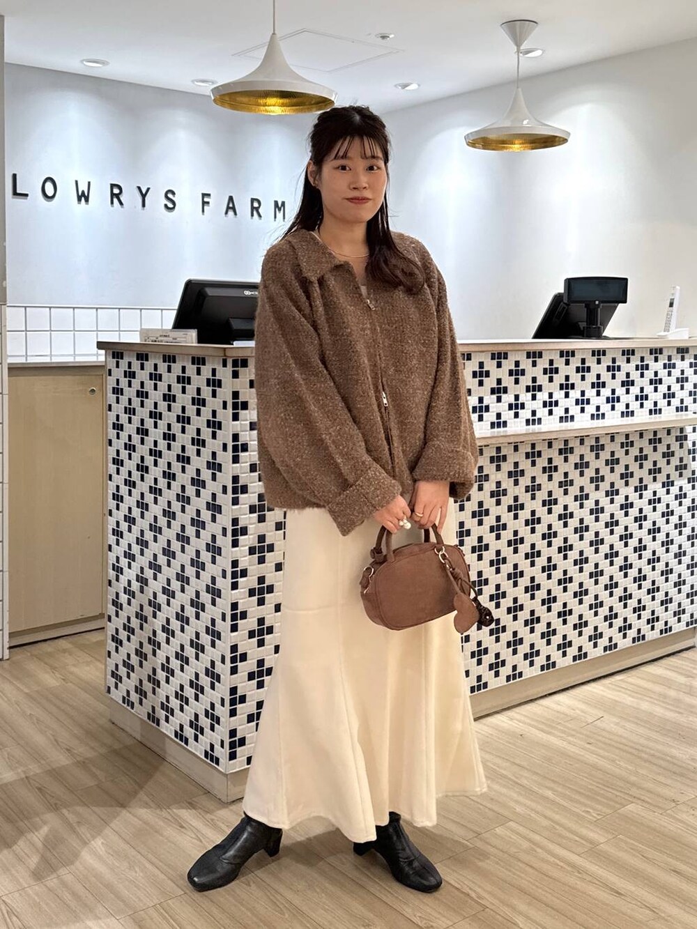 ホワイト系のスカート、ブラウン系のボストンバッグ、ブラウン系のブルゾンを着用したレディースの秋コーディネートの2枚目の写真