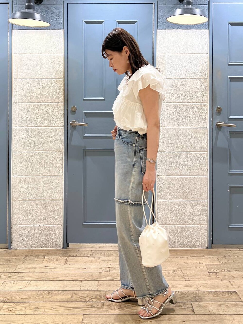 ホワイト系のショルダーバッグ、シルバー系のサンダル、ブルー系のデニムパンツを着用したレディースの夏コーディネートの2枚目の写真