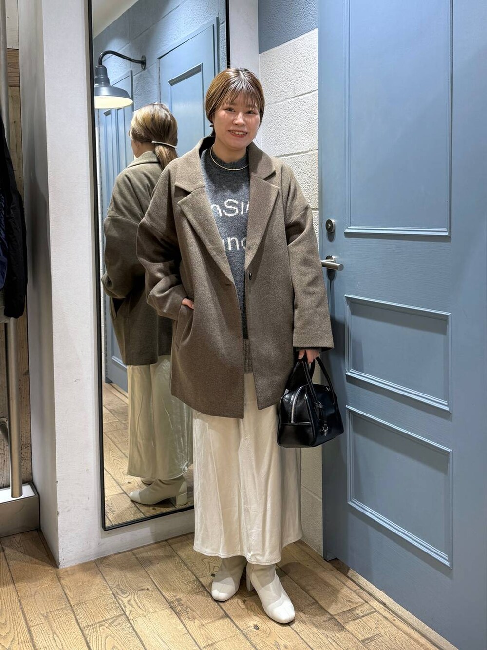 ブラウン系のチェスターコート、ホワイト系のブーツ、ブラック系のボストンバッグを着用したレディースの秋コーディネートの2枚目の写真