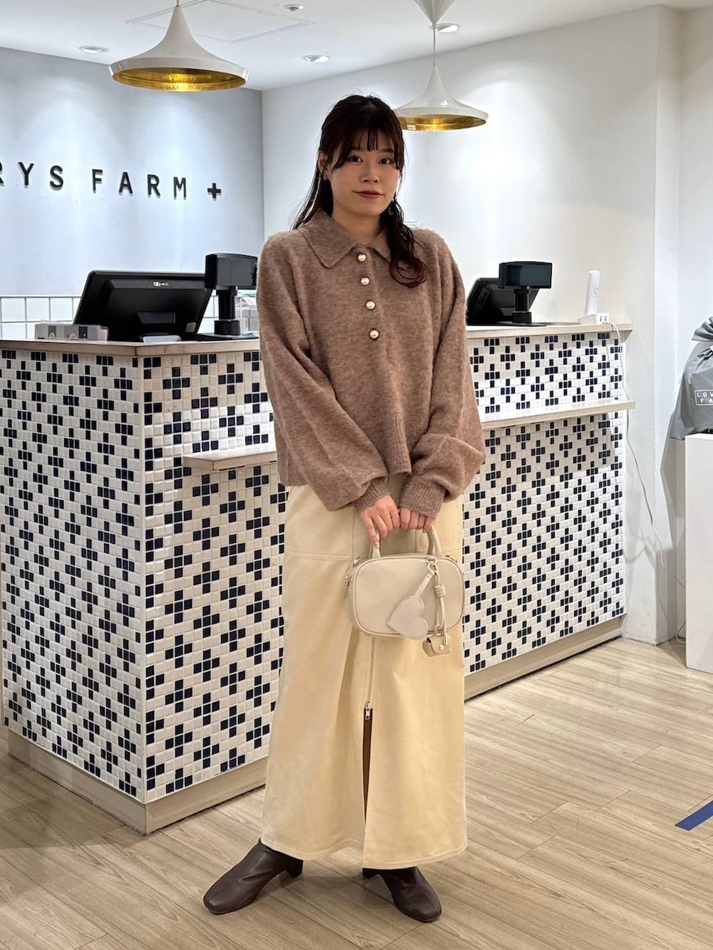 ホワイト系のスカート、ホワイト系のボストンバッグ、ブラウン系のブーツを着用したレディースの冬コーディネートの2枚目の写真