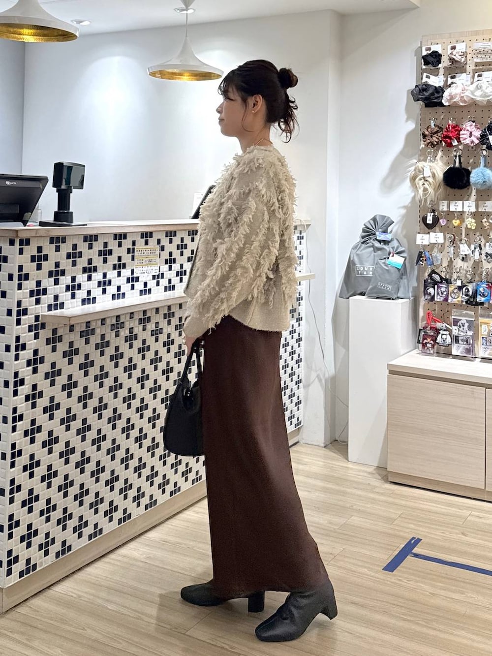 ブラウン系のスカート、ブラック系のショルダーバッグ、ベージュ系のカーディガン/ボレロを着用したレディースの冬コーディネートの4枚目の写真