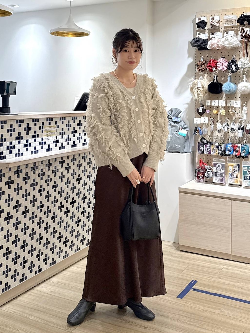 ブラウン系のスカート、ブラック系のショルダーバッグ、ベージュ系のカーディガン/ボレロを着用したレディースの冬コーディネートの3枚目の写真