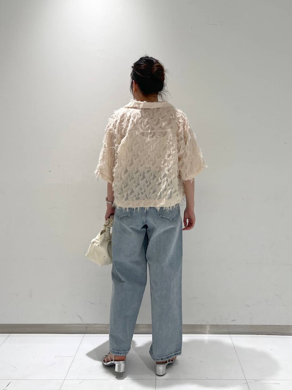ブルー系のデニムパンツ、ベージュ系のハンドバッグ、ホワイト系のキャミソールを着用したレディースの夏コーディネートの3枚目の写真