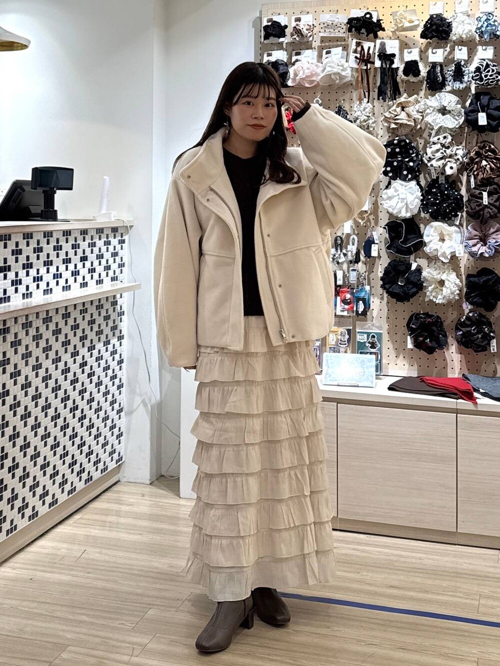 ホワイト系のブルゾン、ホワイト系のスカート、ブラウン系のポロシャツを着用したレディースの秋コーディネートの2枚目の写真