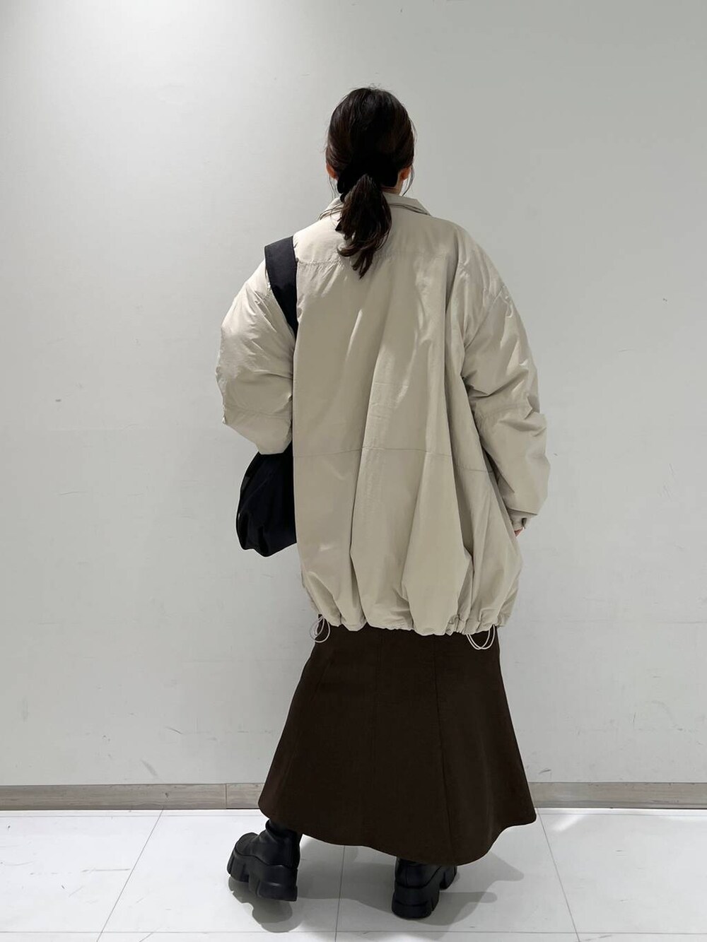 ブラウン系のスカート、ブラック系のブーツ、ホワイト系のダウンジャケット/コートを着用したレディースの冬コーディネートの5枚目の写真