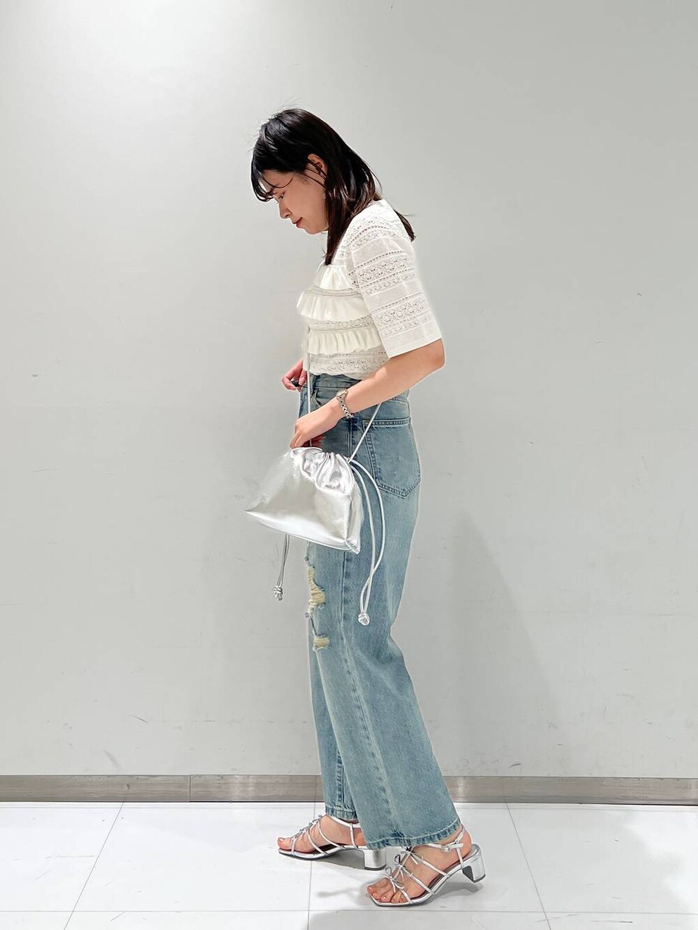 シルバー系のサンダル、シルバー系のショルダーバッグ、ブルー系のデニムパンツを着用したレディースの春コーディネートの2枚目の写真