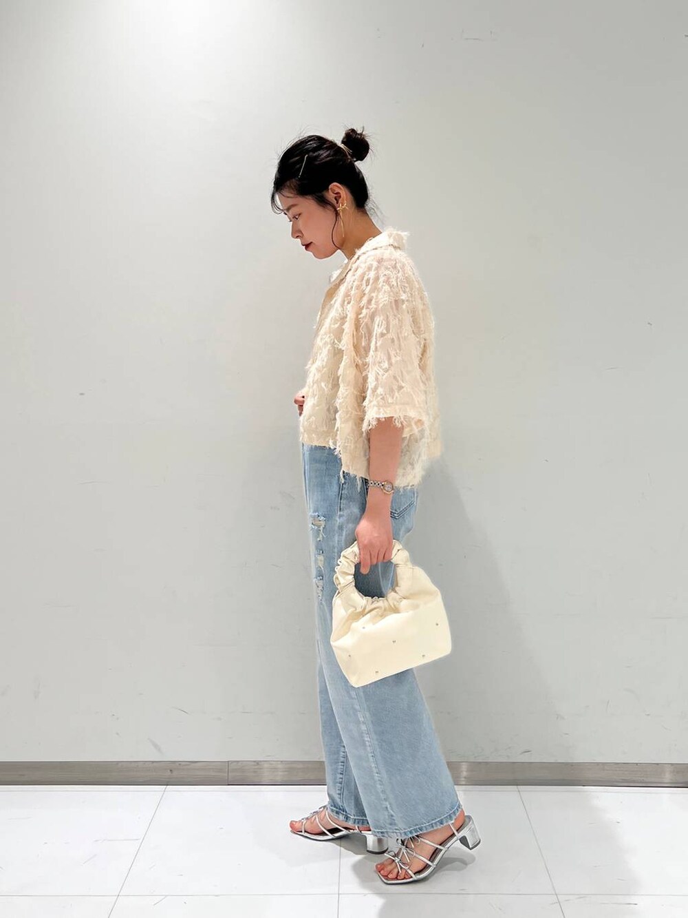 ブルー系のデニムパンツ、ベージュ系のハンドバッグ、ホワイト系のキャミソールを着用したレディースの夏コーディネートの2枚目の写真