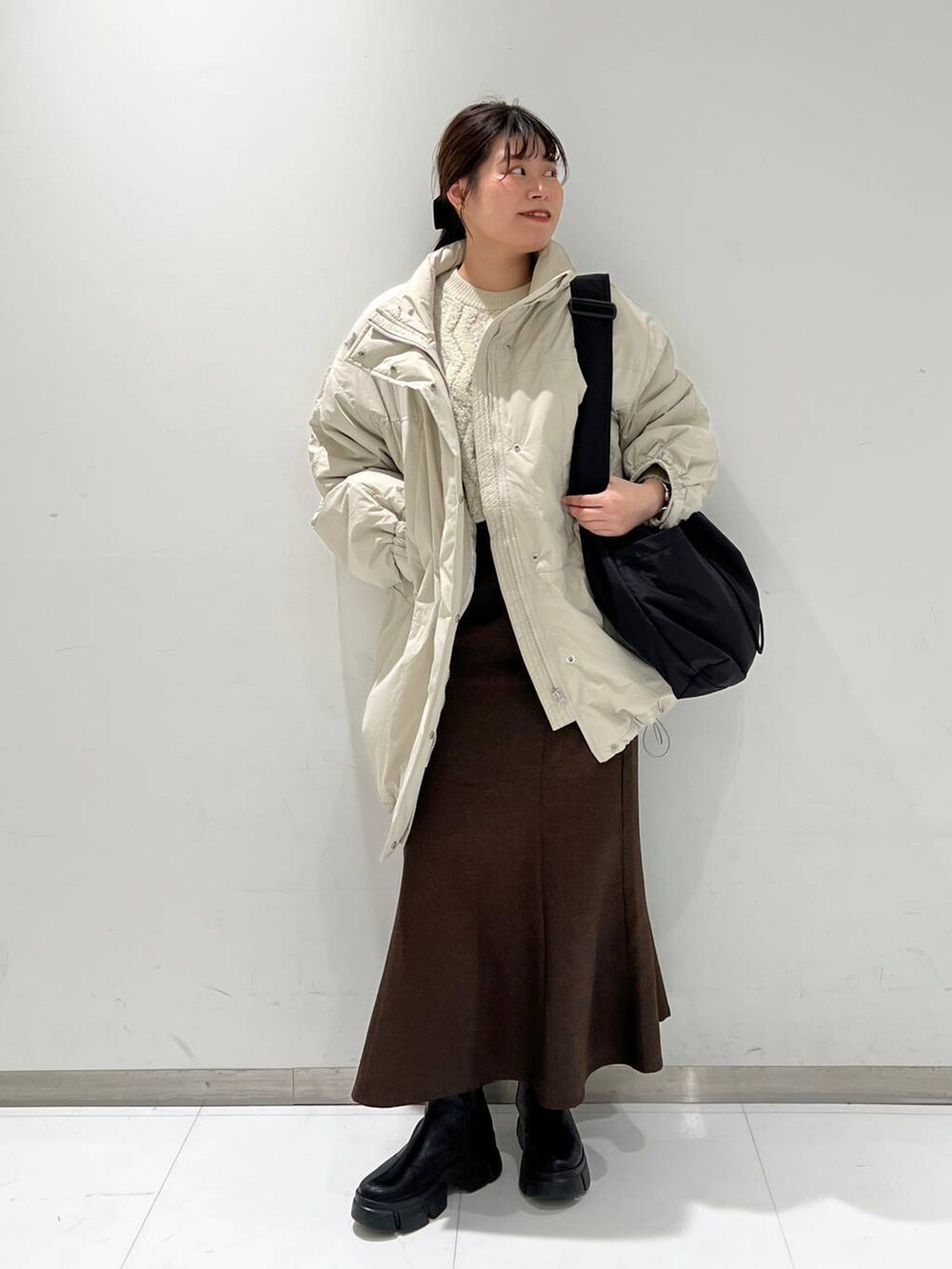 ブラウン系のスカート、ブラック系のブーツ、ホワイト系のダウンジャケット/コートを着用したレディースの冬コーディネートの2枚目の写真