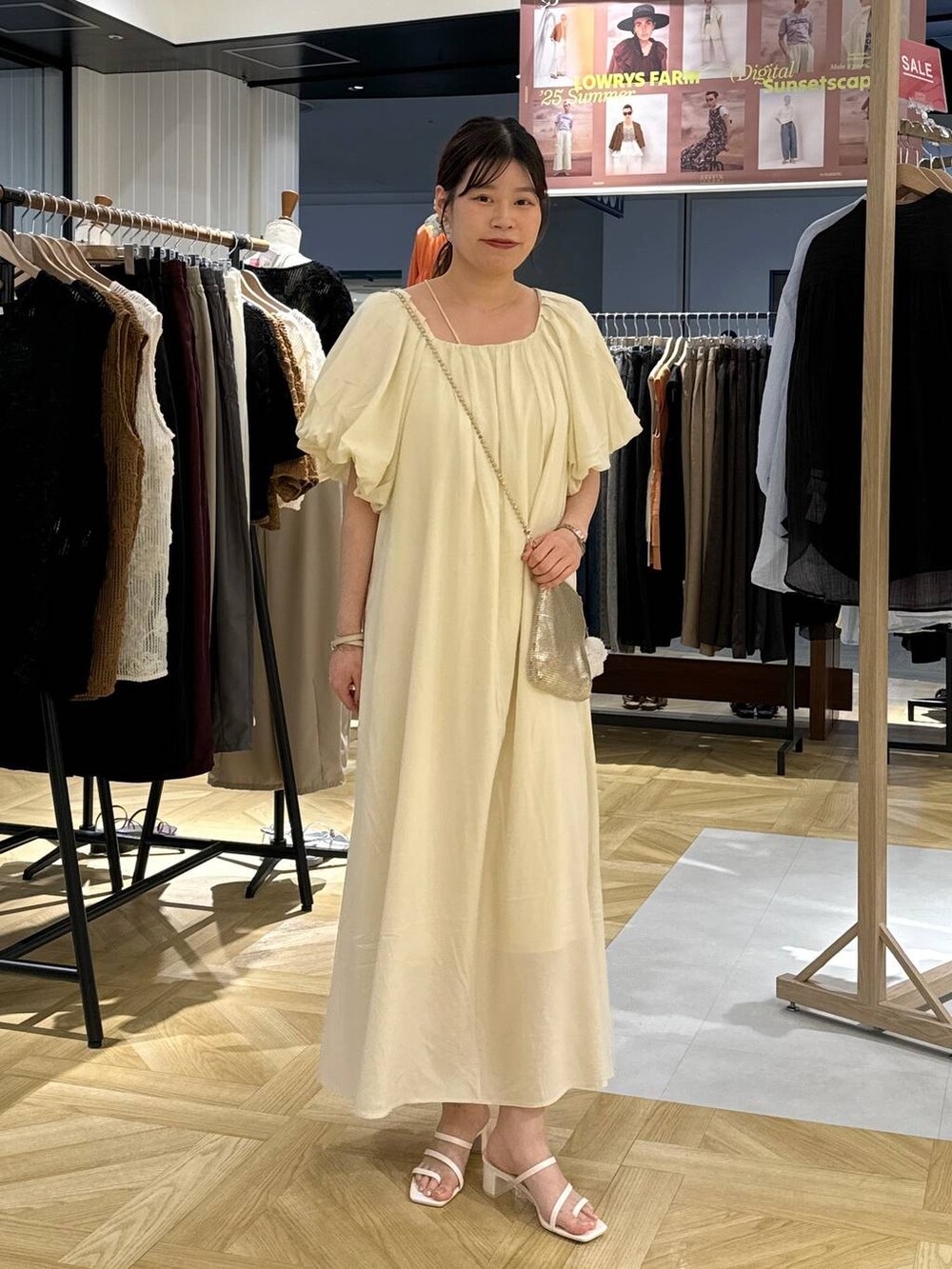 ゴールド系のショルダーバッグ、ホワイト系のサンダル、ホワイト系のワンピースを着用したレディースの夏コーディネートの2枚目の写真