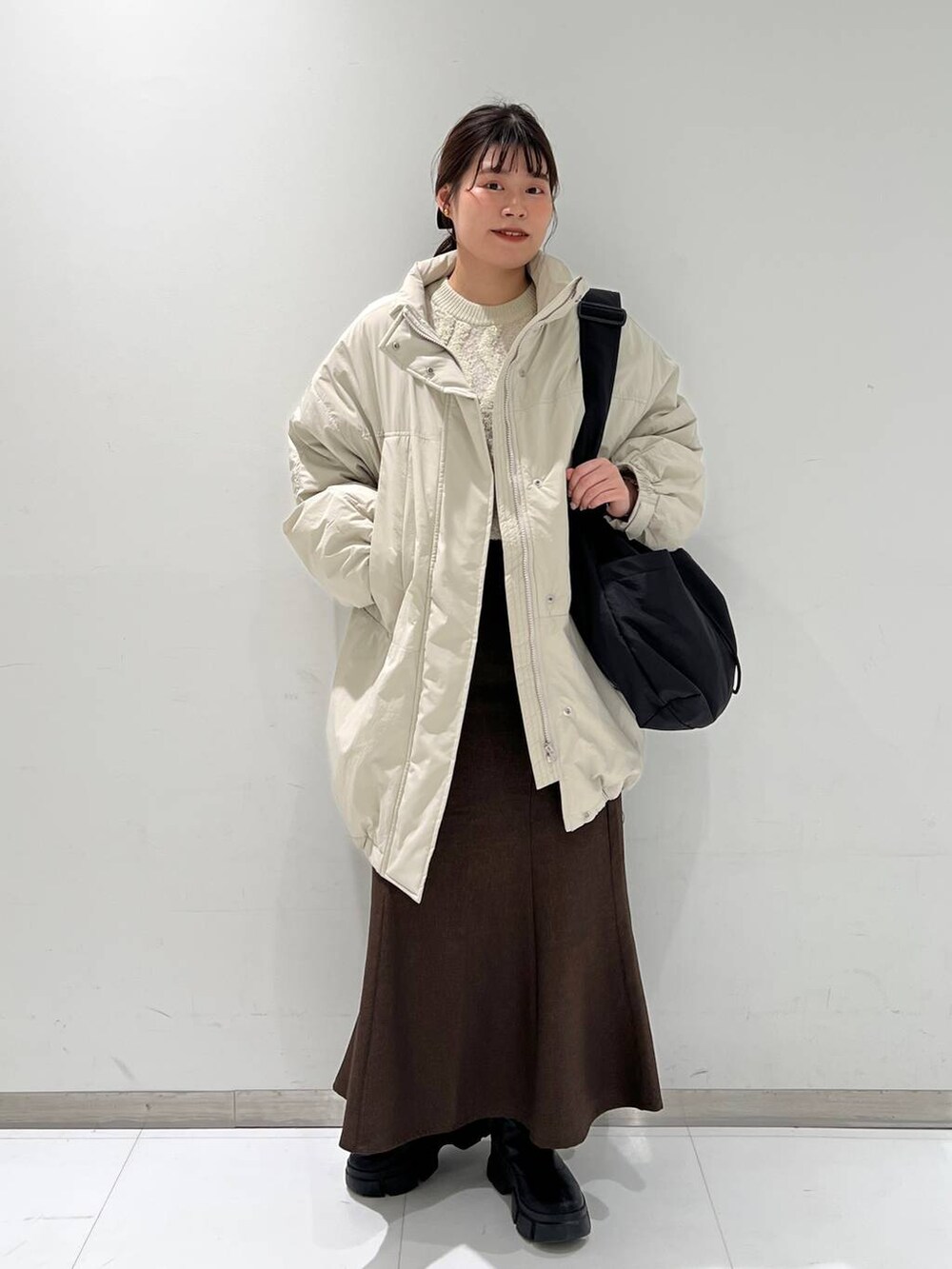 ブラウン系のスカート、ブラック系のブーツ、ホワイト系のダウンジャケット/コートを着用したレディースの冬コーディネートの3枚目の写真