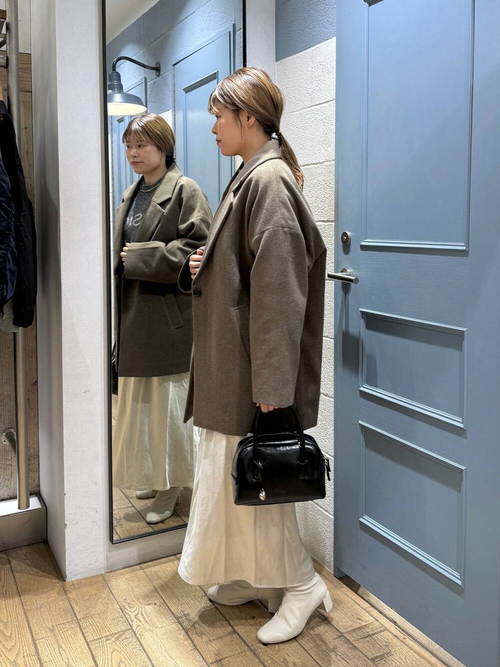 ブラウン系のチェスターコート、ホワイト系のブーツ、ブラック系のボストンバッグを着用したレディースの秋コーディネートの3枚目の写真