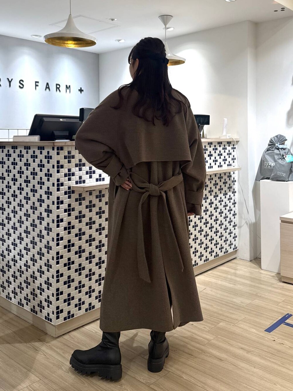 ブラウン系のステンカラーコート、ブラウン系のその他パンツ、ブラック系のブーツを着用したレディースの秋コーディネートの5枚目の写真