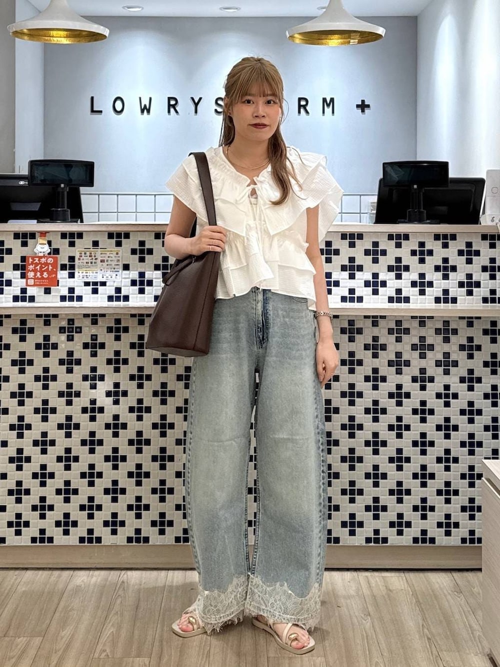ブルー系のデニムパンツ、ホワイト系のサンダル、ブラウン系のトートバッグを着用したレディースの夏コーディネートの2枚目の写真