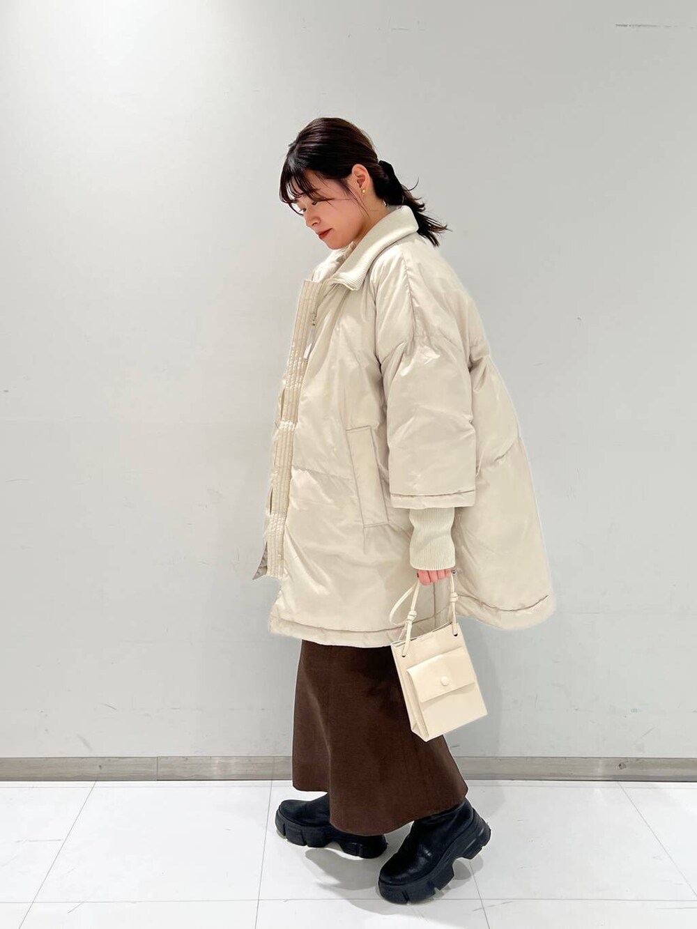 ホワイト系のショルダーバッグ、ブラウン系のスカート、ブラック系のブーツを着用したレディースの冬コーディネートの2枚目の写真