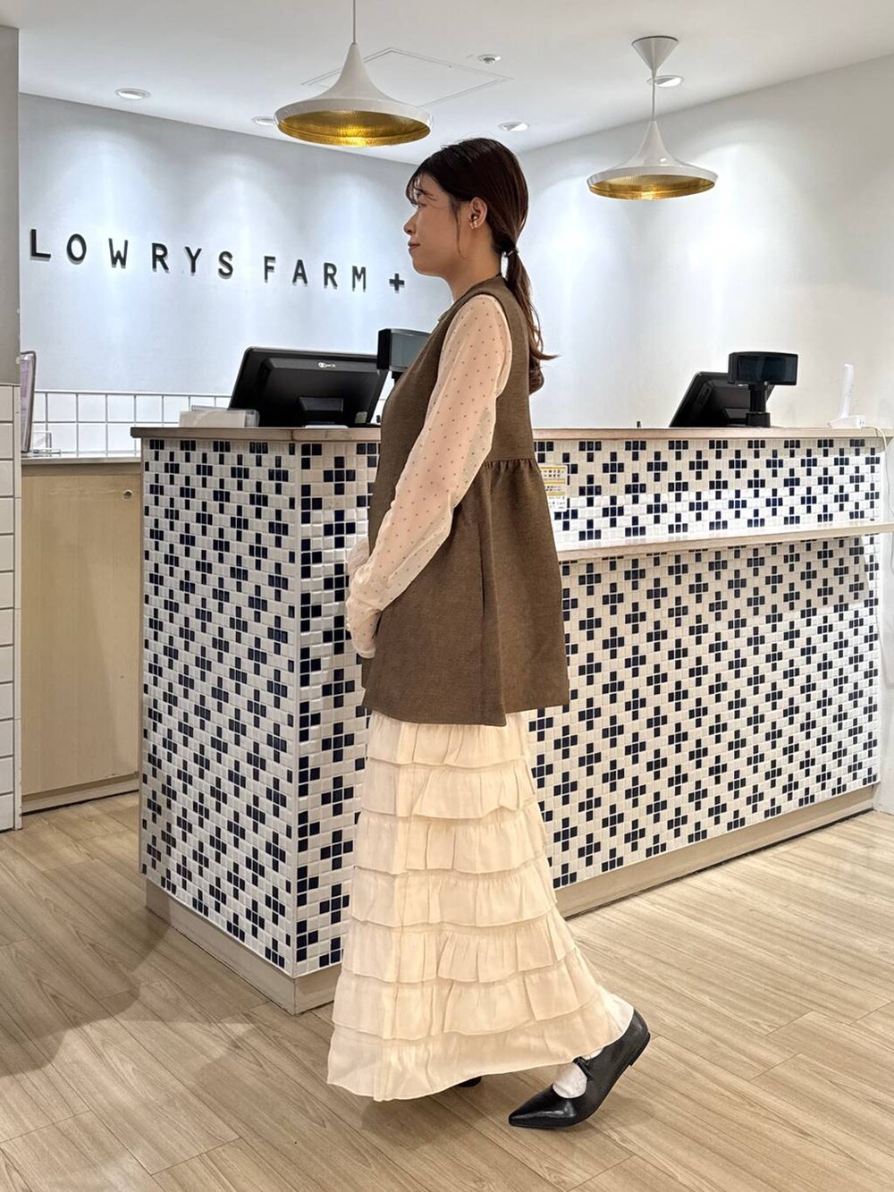ブラウン系のベスト、ホワイト系のスカート、ブラック系のパンプスを着用したレディースの秋コーディネートの3枚目の写真