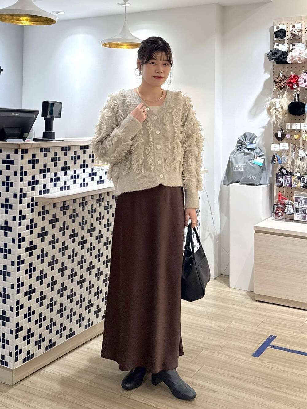 ブラウン系のスカート、ブラック系のショルダーバッグ、ベージュ系のカーディガン/ボレロを着用したレディースの冬コーディネートの2枚目の写真