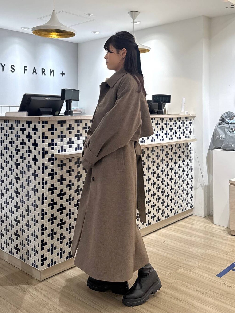 ブラウン系のステンカラーコート、ブラウン系のその他パンツ、ブラック系のブーツを着用したレディースの秋コーディネートの4枚目の写真