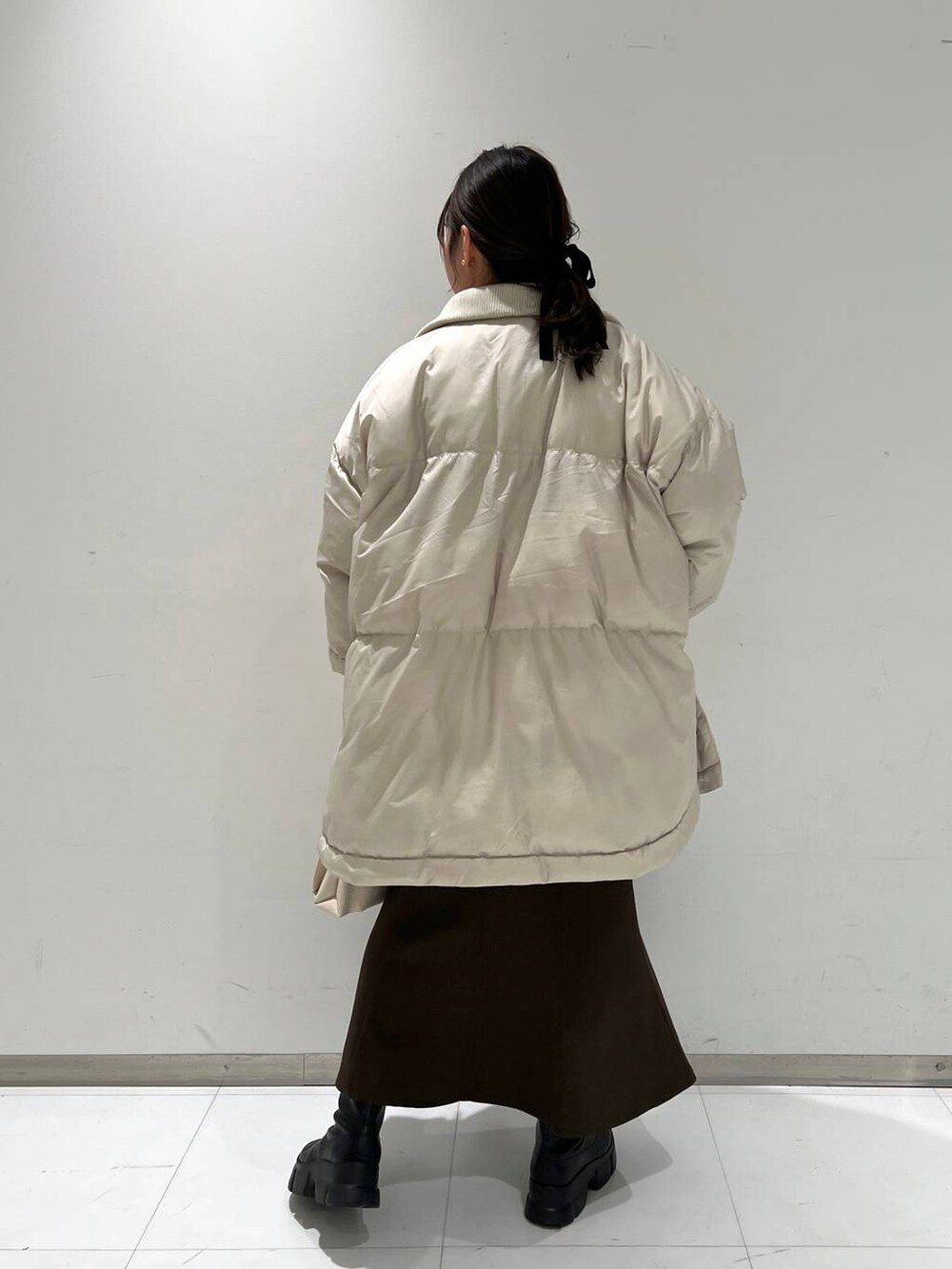 ホワイト系のショルダーバッグ、ブラウン系のスカート、ブラック系のブーツを着用したレディースの冬コーディネートの3枚目の写真