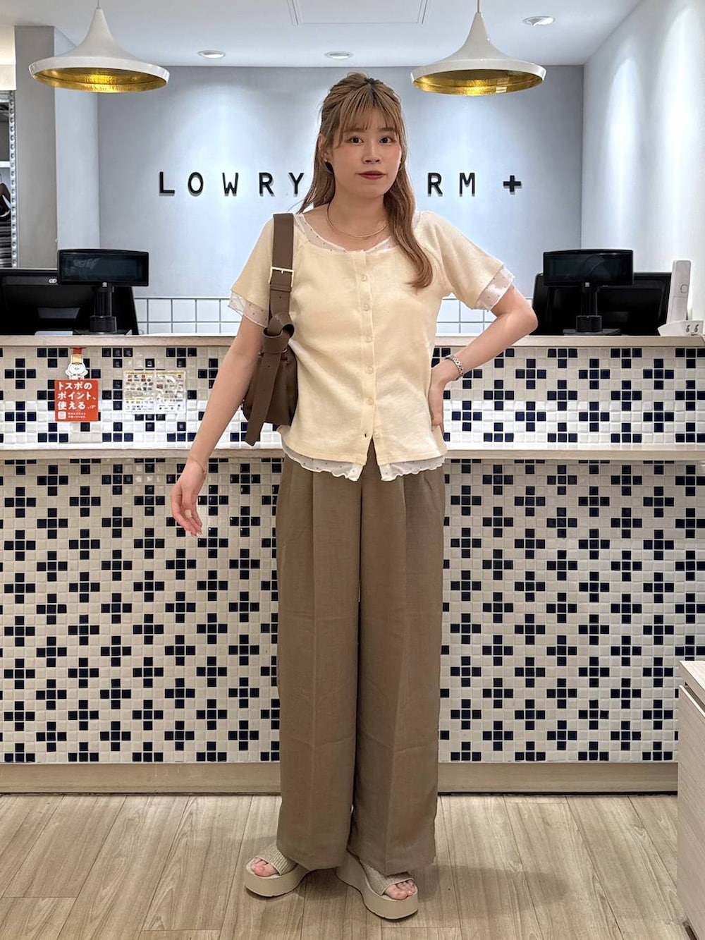 ベージュ系のスラックス、ホワイト系のサンダル、ブラウン系のショルダーバッグを着用したレディースの夏コーディネートの2枚目の写真