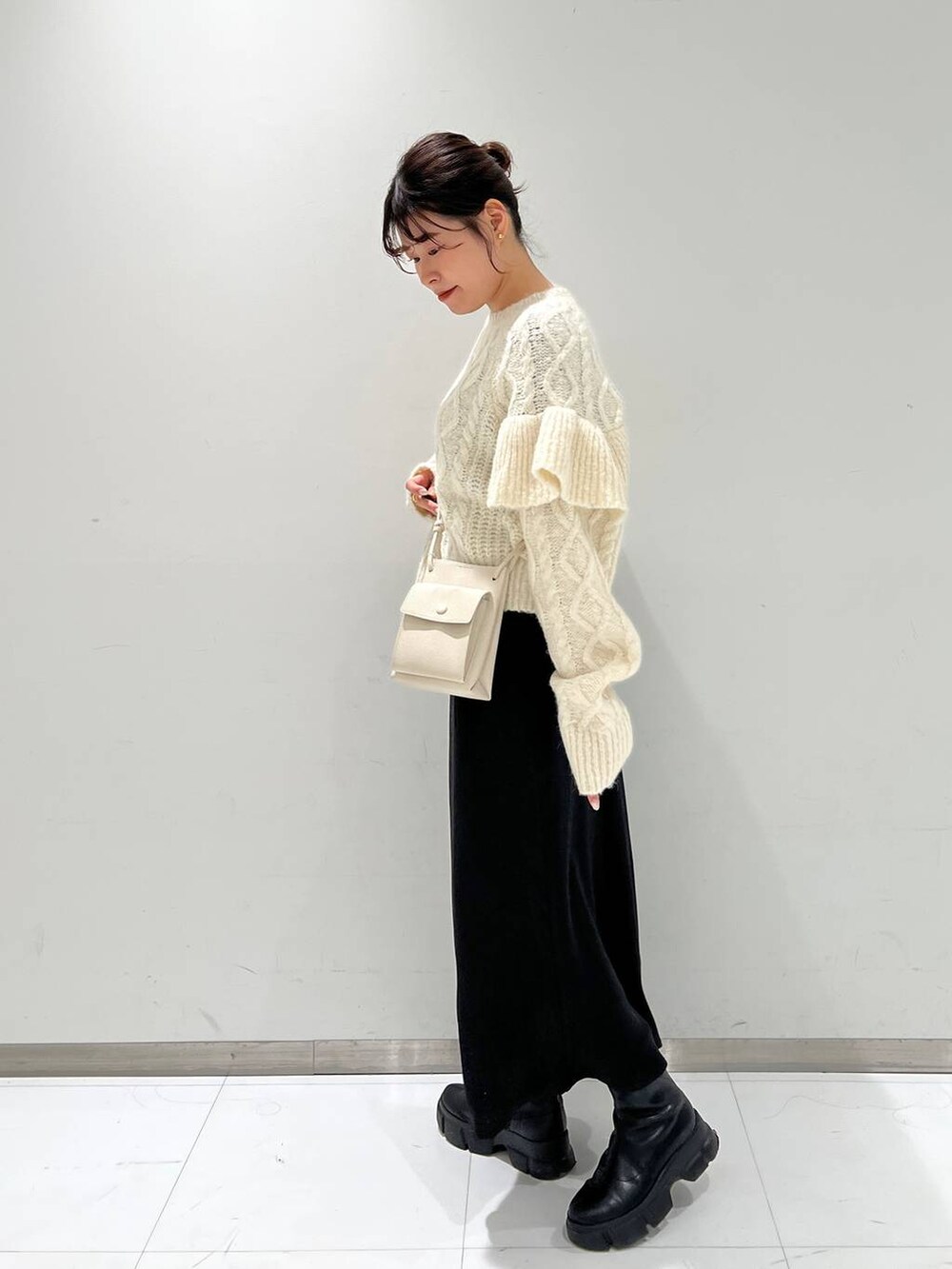 ホワイト系のショルダーバッグ、ブラック系のブーツ、ホワイト系のニット/セーターを着用したレディースの冬コーディネートの2枚目の写真