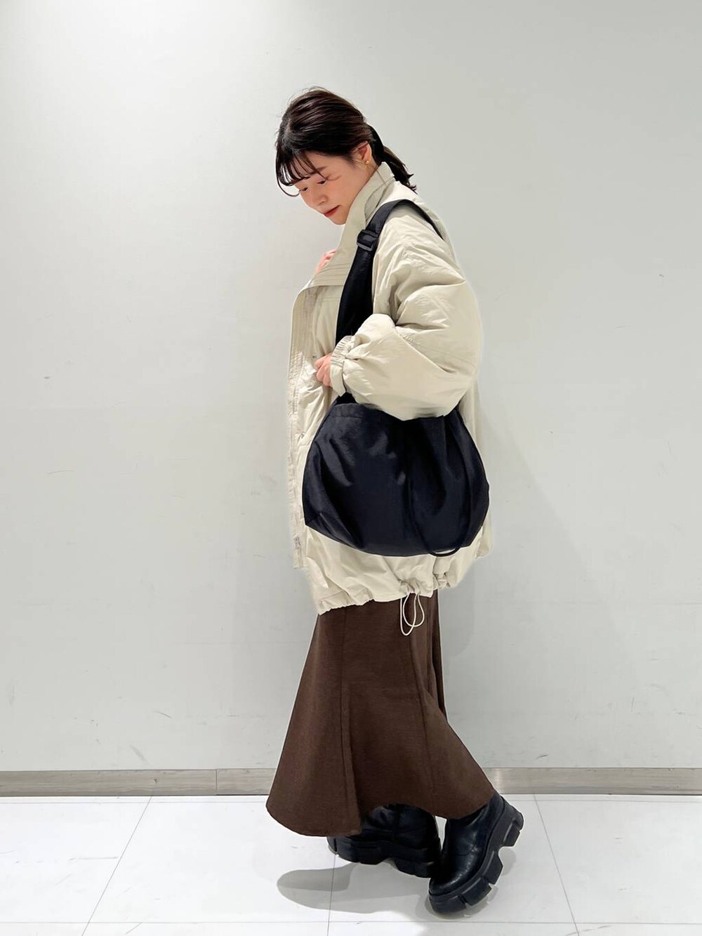 ブラウン系のスカート、ブラック系のブーツ、ホワイト系のダウンジャケット/コートを着用したレディースの冬コーディネートの4枚目の写真