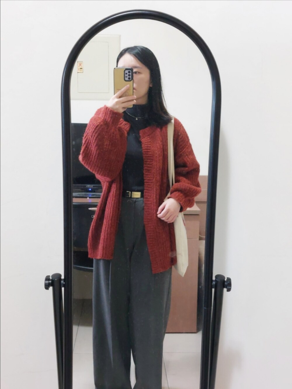 レッド系のカーディガン/ボレロ、グレー系のスラックス、ゴールド系のピアス（片耳用）を着用したレディースの冬コーディネートの2枚目の写真