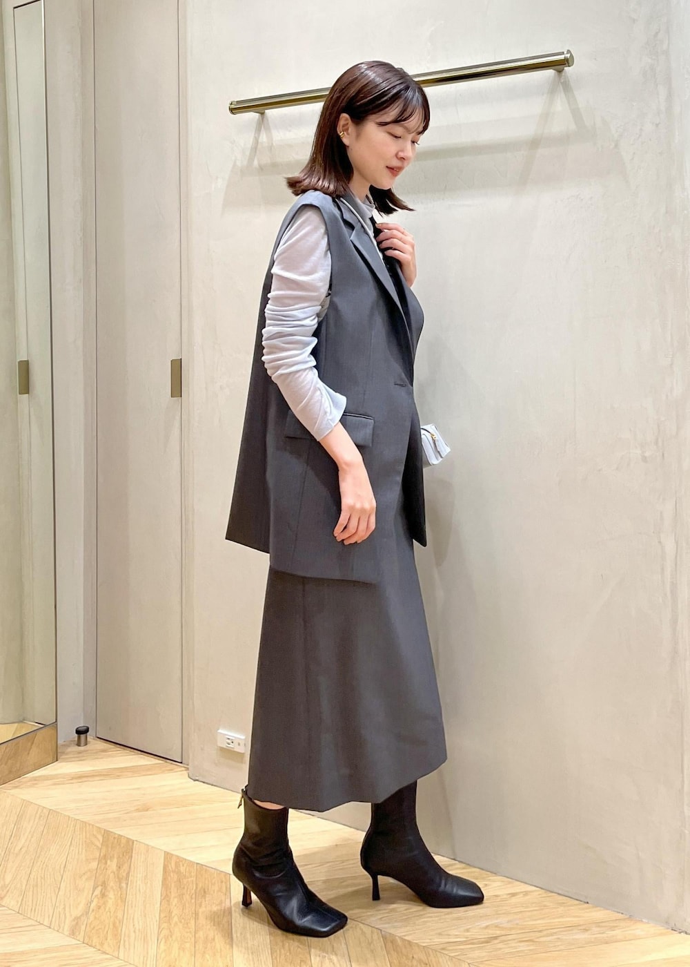 ブラック系のブーツ、ブルー系のショルダーバッグ、グレー系のベストを着用したレディースの秋コーディネートの2枚目の写真