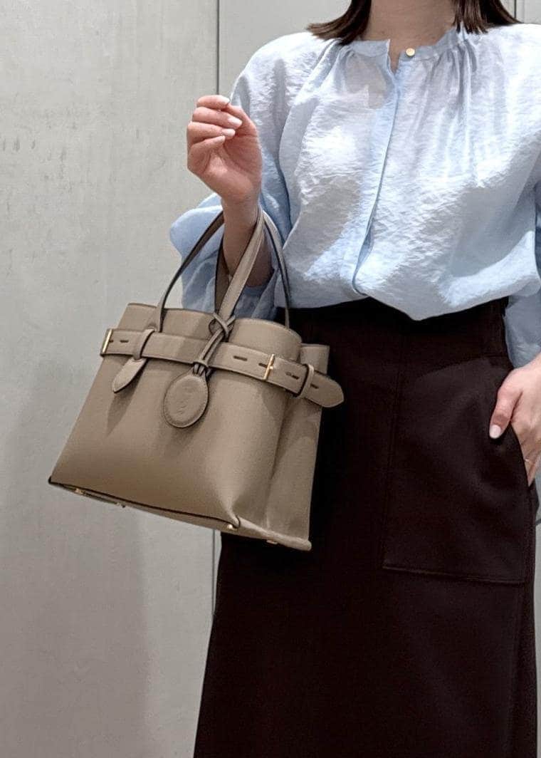 ブラウン系のスカート、ベージュ系のハンドバッグ、ブルー系のシャツ/ブラウスを着用したレディースの春コーディネートの8枚目の写真