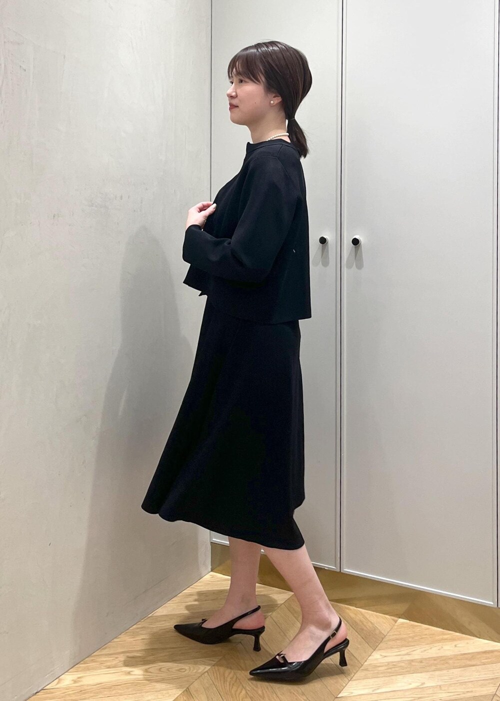ブラック系のハンドバッグ、ブラック系のパンプス、ブルー系のワンピースを着用したレディースの冬コーディネートの2枚目の写真