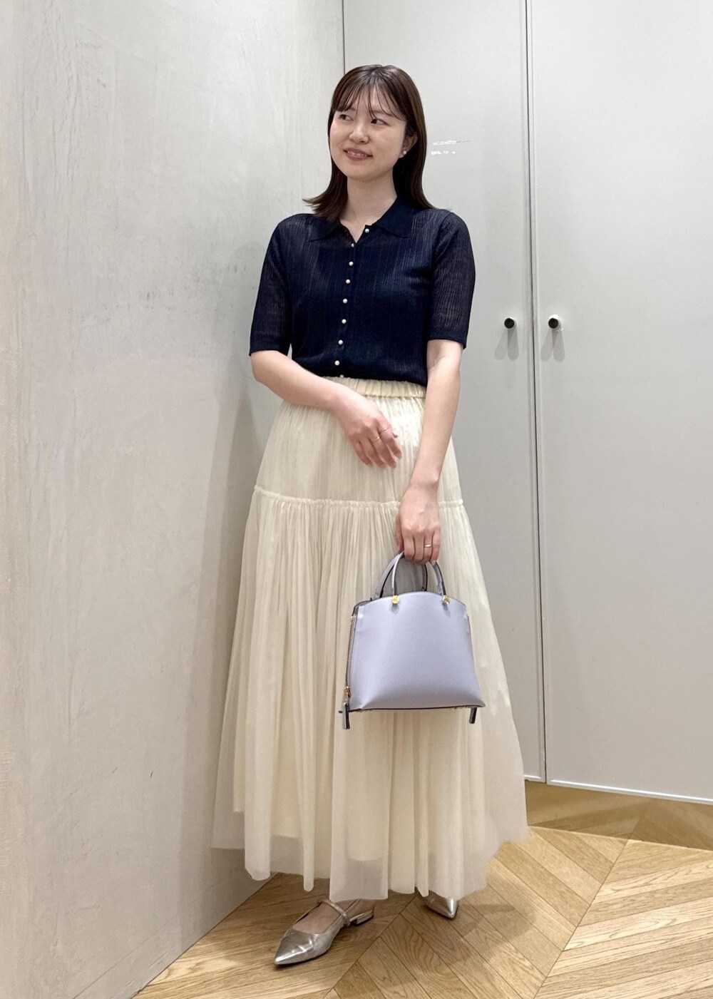 パープル系のハンドバッグ、ベージュ系のスカート、ブルー系のカーディガン/ボレロを着用したレディースの春コーディネートの2枚目の写真