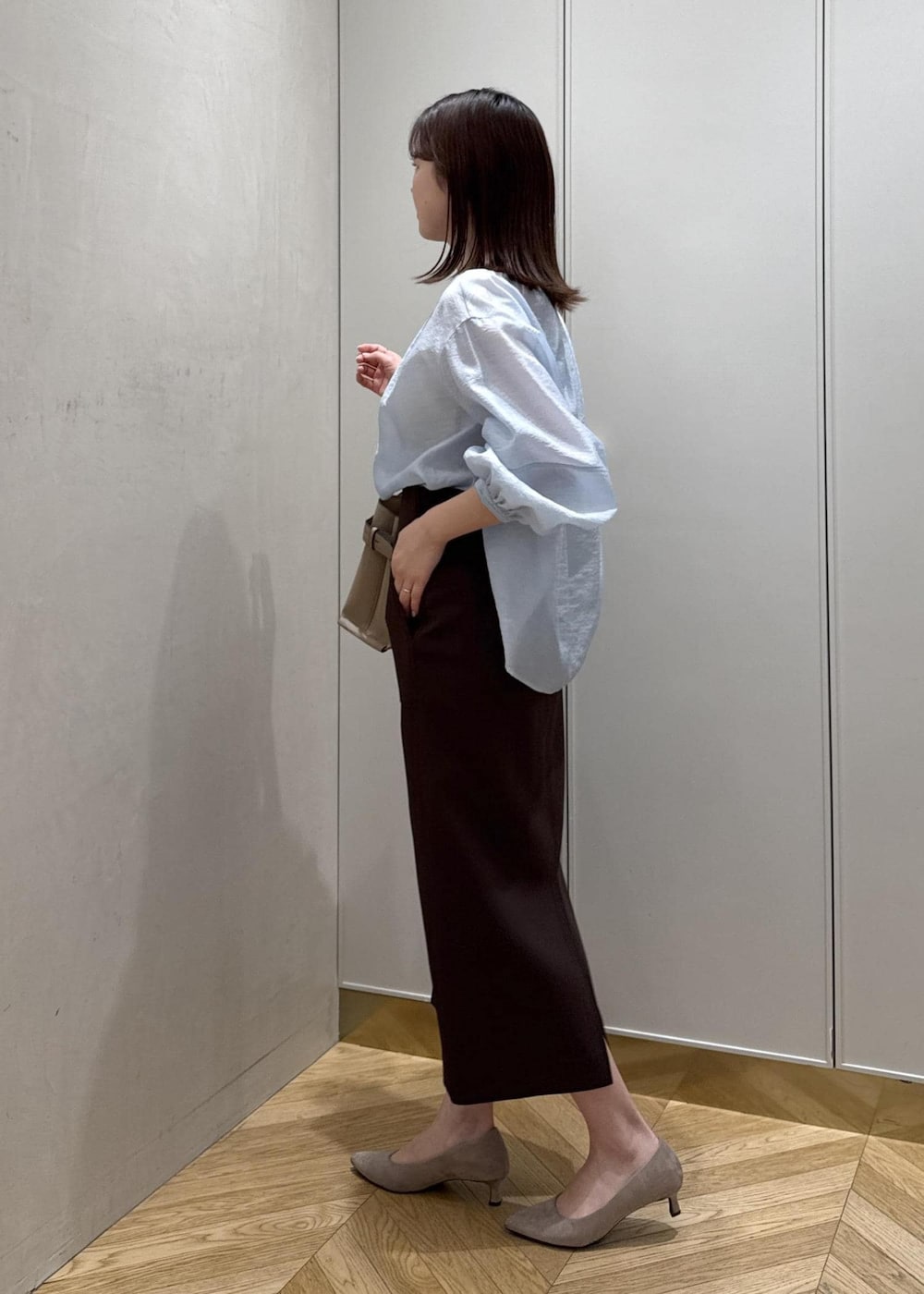 ブラウン系のスカート、ベージュ系のハンドバッグ、ブルー系のシャツ/ブラウスを着用したレディースの春コーディネートの2枚目の写真