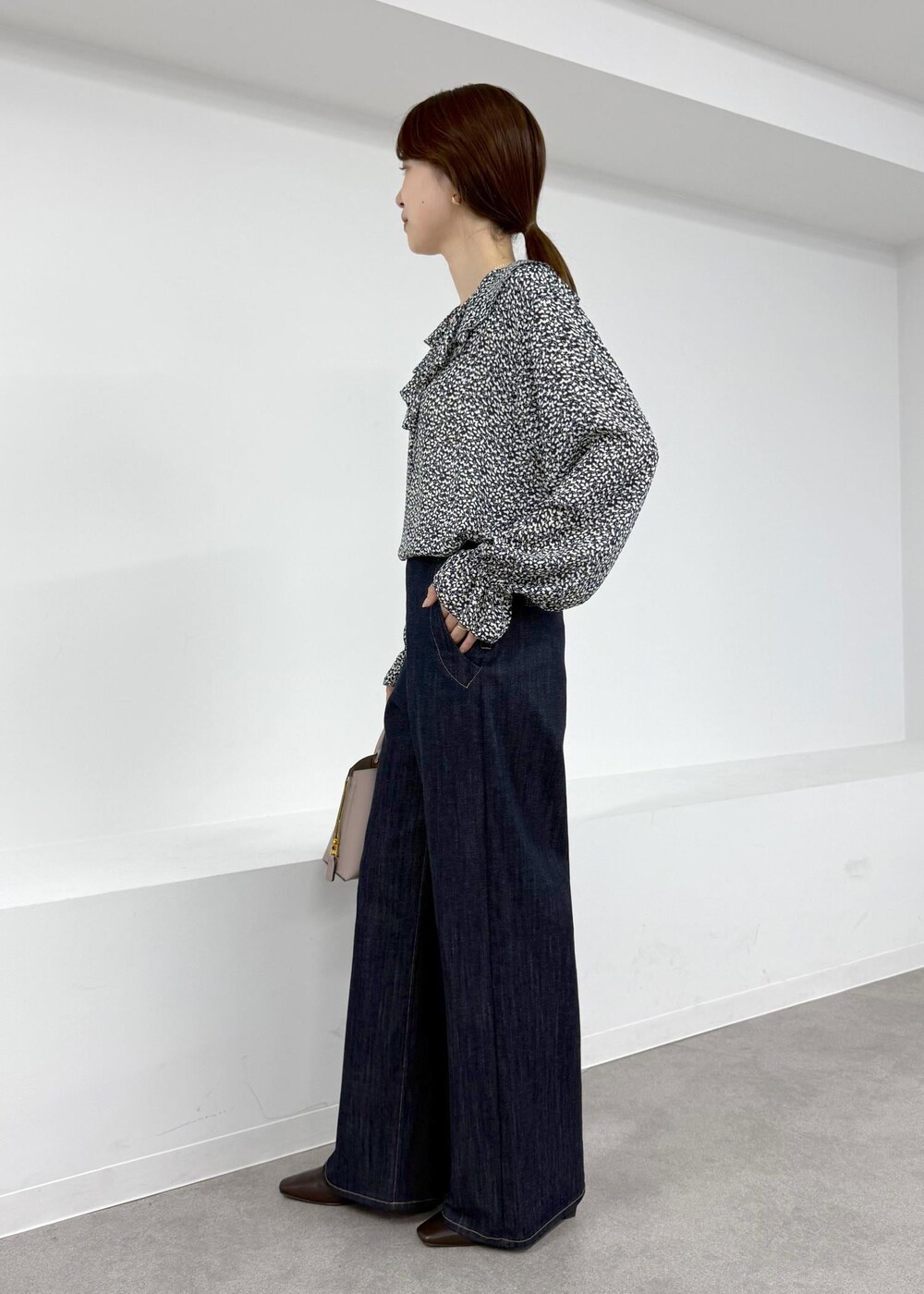 グレー系のハンドバッグ、ブラウン系のブーツ、ブルー系のデニムパンツを着用したレディースの秋コーディネートの2枚目の写真