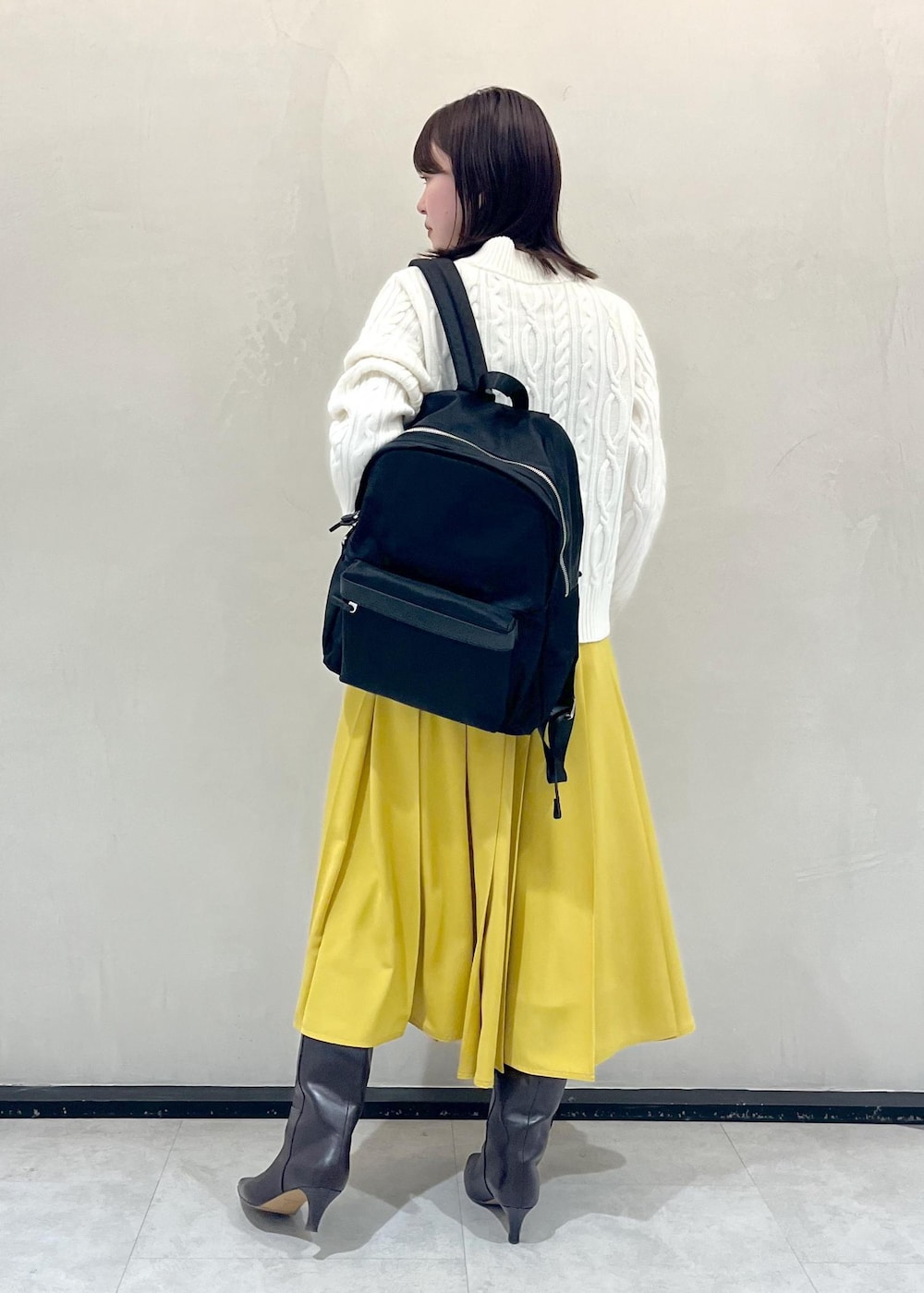 ブラウン系のブーツ、イエロー系のスカート、ブラック系のバックパック/リュックを着用したレディースの冬コーディネートの3枚目の写真