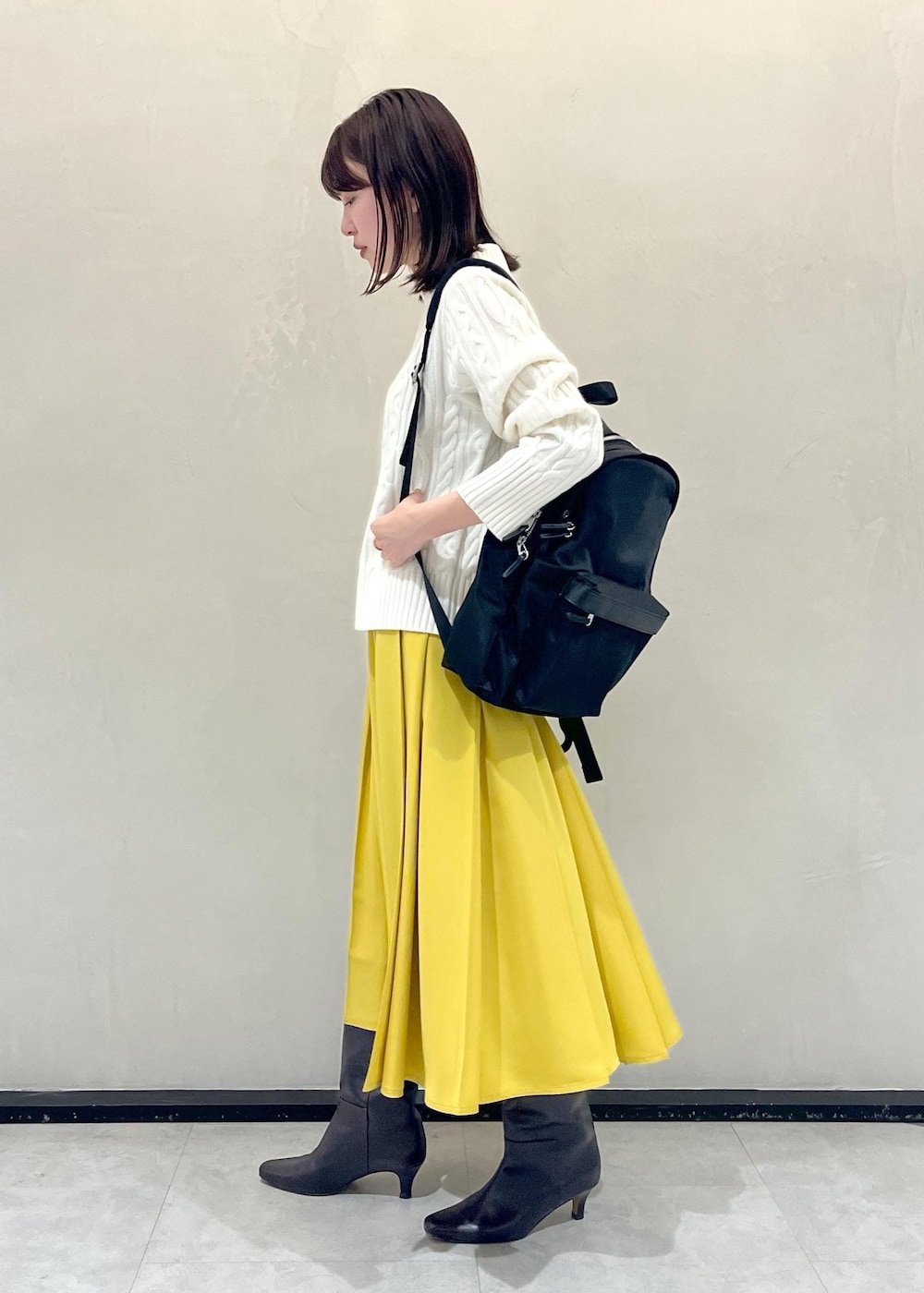 ブラウン系のブーツ、イエロー系のスカート、ブラック系のバックパック/リュックを着用したレディースの冬コーディネートの2枚目の写真