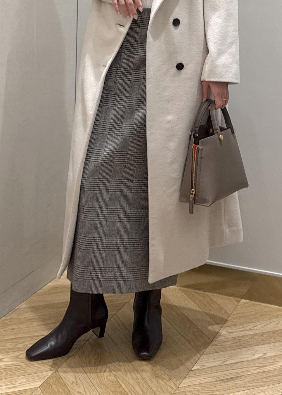 ブラウン系のブーツ、ブラウン系のハンドバッグ、ホワイト系のステンカラーコートを着用したレディースの秋コーディネートの7枚目の写真