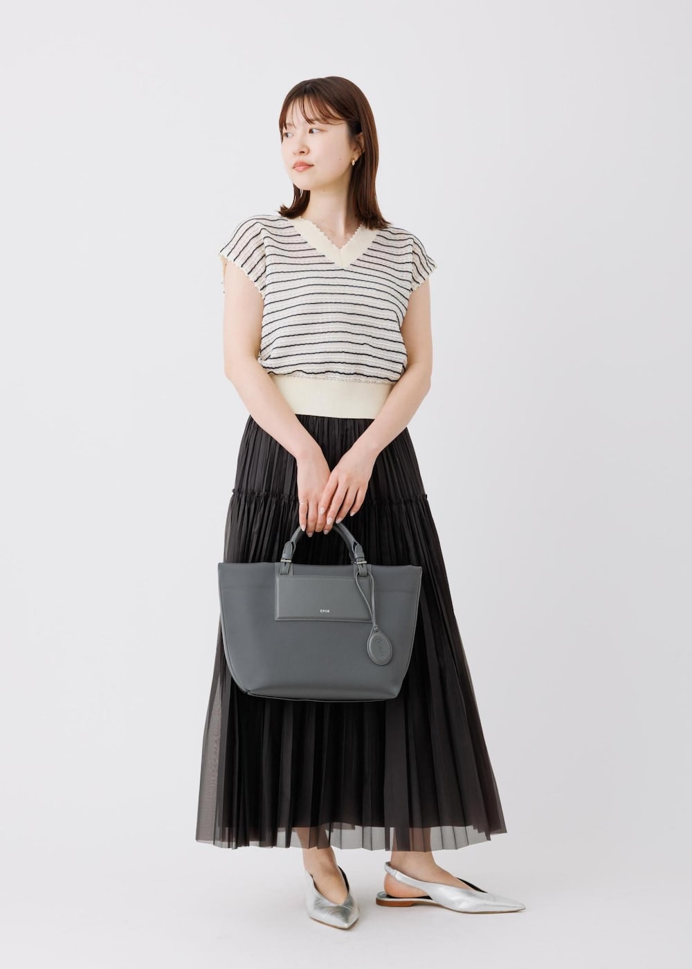 ブラック系のスカート、ホワイト系のニット/セーター、グレー系のトートバッグを着用したレディースの春コーディネートの2枚目の写真