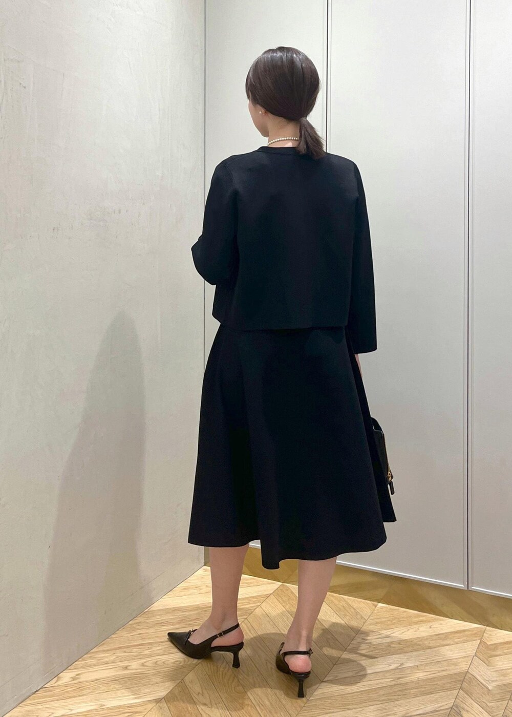 ブラック系のハンドバッグ、ブラック系のパンプス、ブルー系のワンピースを着用したレディースの冬コーディネートの3枚目の写真