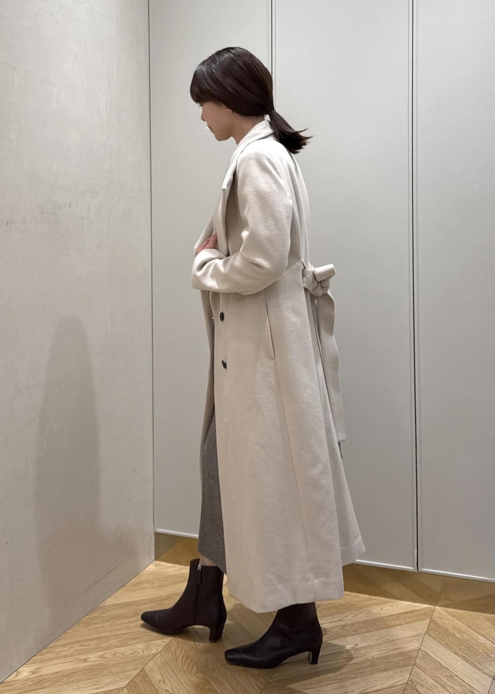 ブラウン系のブーツ、ブラウン系のハンドバッグ、ホワイト系のステンカラーコートを着用したレディースの秋コーディネートの2枚目の写真