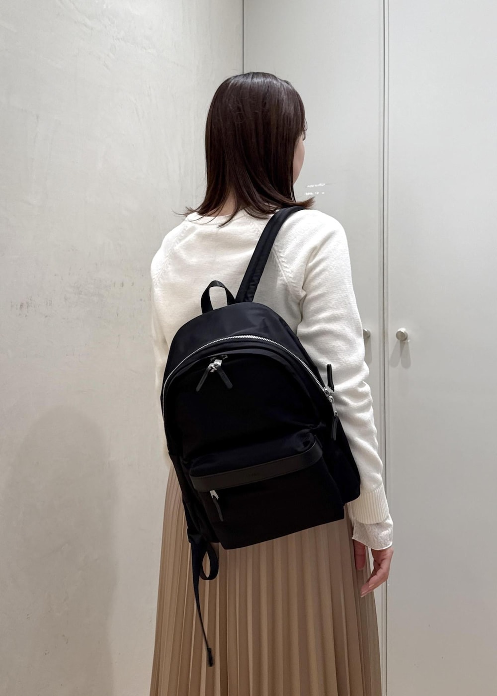 ブラック系のバックパック/リュック、ホワイト系のTシャツ/カットソー、ベージュ系のスカートを着用したレディースの春コーディネートの7枚目の写真