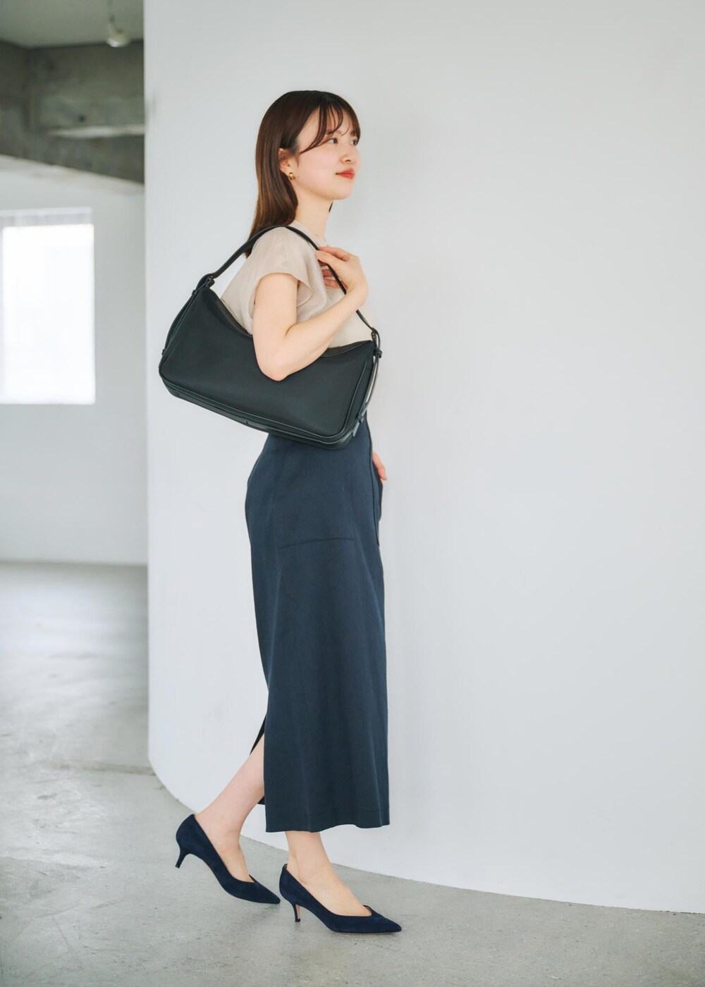 ブルー系のスカート、ブラック系のハンドバッグ、ベージュ系のシャツ/ブラウスを着用したレディースの春コーディネートの2枚目の写真